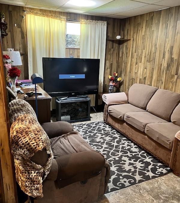 living room with a paneled ceiling and wood walls