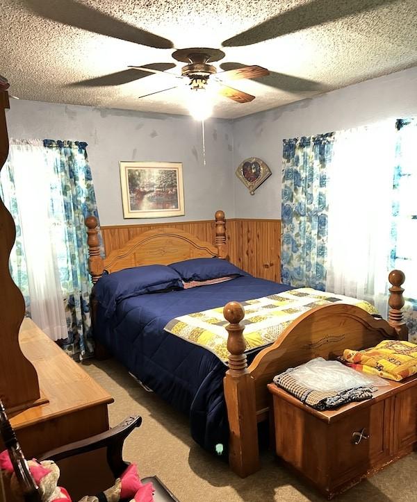 carpeted bedroom featuring wooden walls, ceiling fan, and a textured ceiling