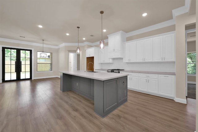 kitchen featuring tasteful backsplash, white cabinets, a center island with sink, sink, and hardwood / wood-style flooring