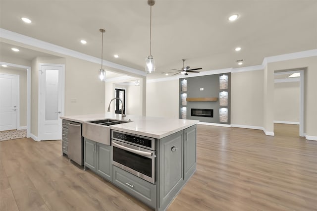 kitchen featuring light hardwood / wood-style flooring, ceiling fan, an island with sink, appliances with stainless steel finishes, and a large fireplace