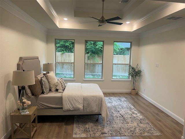 bedroom with multiple windows, hardwood / wood-style floors, and a tray ceiling