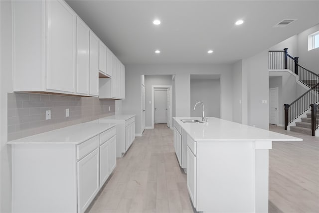 kitchen featuring white cabinetry, a center island with sink, light hardwood / wood-style floors, and sink