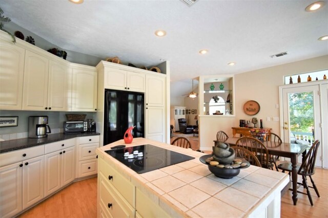 kitchen with light wood-type flooring, black electric stovetop, refrigerator, and tile counters