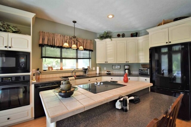 kitchen with light wood-type flooring, a chandelier, tile counters, and black appliances