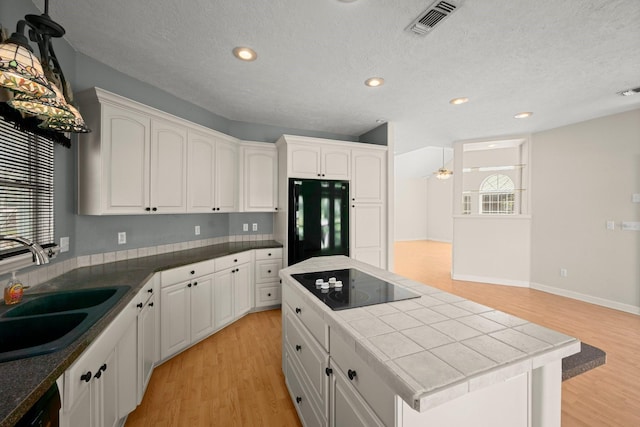 kitchen featuring a sink, tile countertops, black appliances, and light wood-style floors