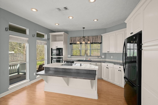 kitchen featuring white cabinets, a kitchen island, a sink, light wood-style floors, and black appliances