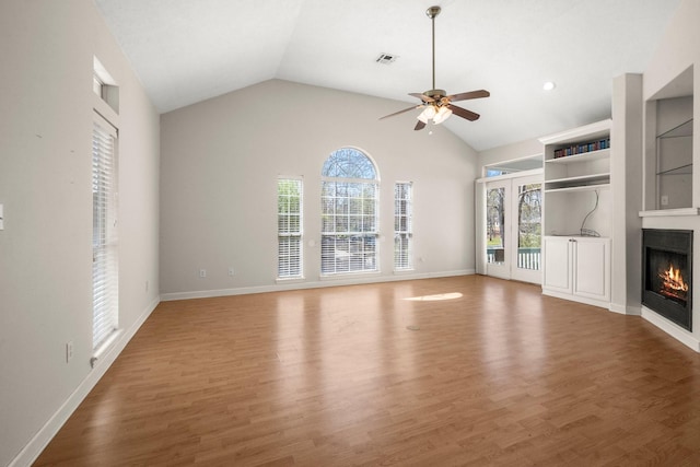 unfurnished living room featuring vaulted ceiling, light wood-style flooring, baseboards, a ceiling fan, and a glass covered fireplace