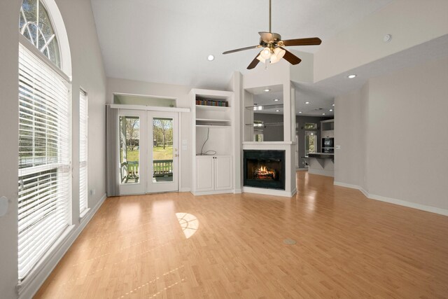 unfurnished living room featuring light wood finished floors, a lit fireplace, high vaulted ceiling, and ceiling fan