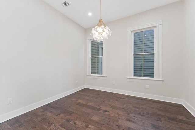 spare room with dark hardwood / wood-style floors and an inviting chandelier