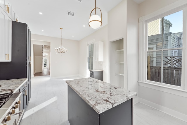 kitchen featuring white cabinetry, a center island, light stone counters, and decorative light fixtures