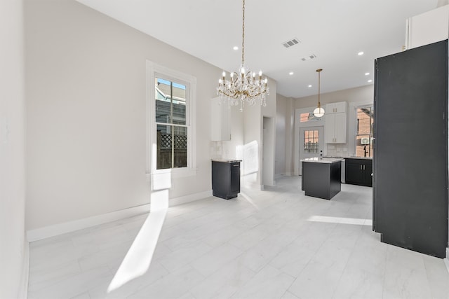 interior space with white cabinetry, a center island, hanging light fixtures, black fridge, and decorative backsplash