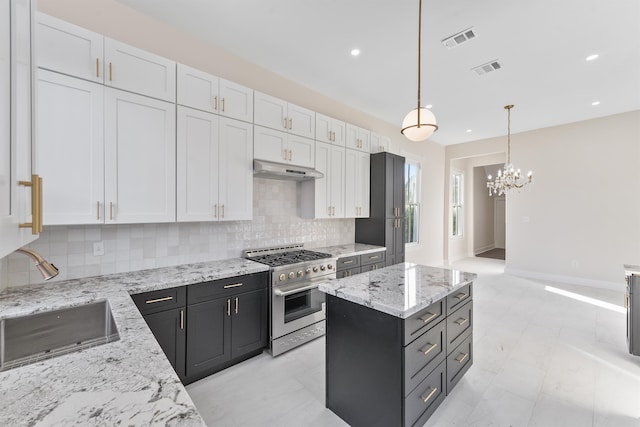 kitchen featuring high end range, sink, hanging light fixtures, light stone counters, and white cabinetry