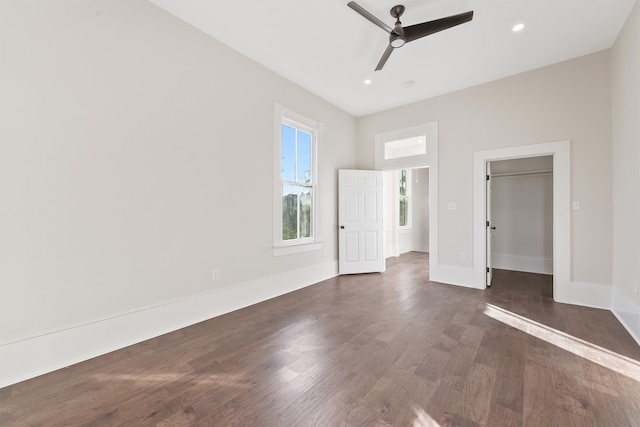 unfurnished bedroom featuring ceiling fan, a walk in closet, dark wood-type flooring, and a closet