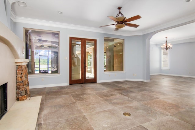 unfurnished living room featuring ceiling fan with notable chandelier, a stone fireplace, crown molding, and french doors