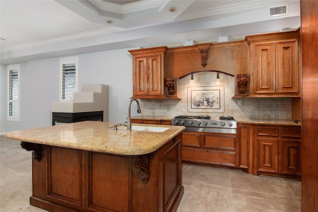 kitchen with stainless steel gas stovetop, an island with sink, tasteful backsplash, sink, and light stone countertops