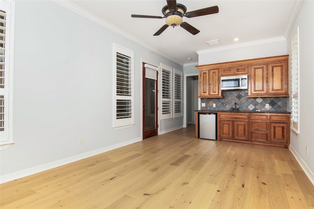 kitchen featuring appliances with stainless steel finishes, backsplash, ornamental molding, sink, and light hardwood / wood-style flooring