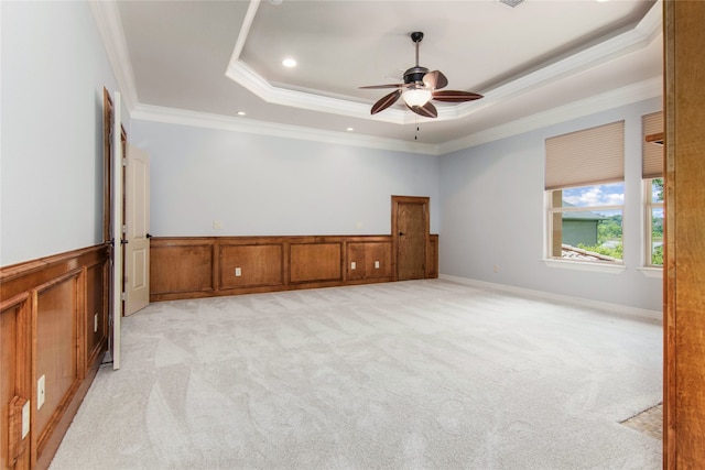 unfurnished room with light colored carpet, ceiling fan, a raised ceiling, and ornamental molding