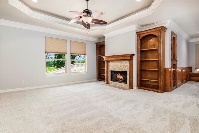 unfurnished living room featuring light carpet, ornamental molding, a raised ceiling, a tile fireplace, and ceiling fan