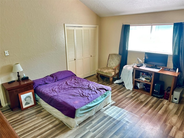 bedroom with a textured ceiling, hardwood / wood-style flooring, vaulted ceiling, and a closet