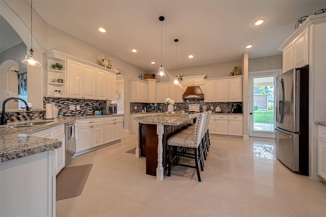 kitchen featuring appliances with stainless steel finishes, sink, white cabinets, hanging light fixtures, and light stone counters