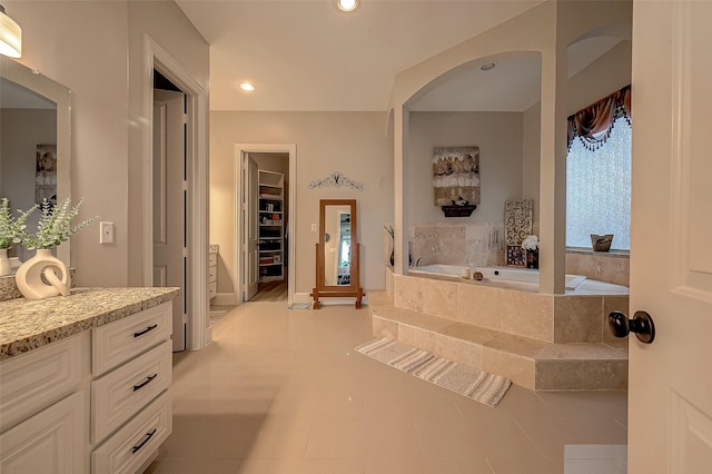 bathroom featuring tile patterned flooring, vanity, and a relaxing tiled tub