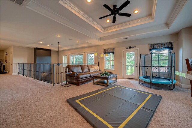 carpeted living room with a raised ceiling, ornamental molding, and ceiling fan