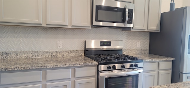 kitchen with light stone countertops, white cabinets, backsplash, and stainless steel appliances