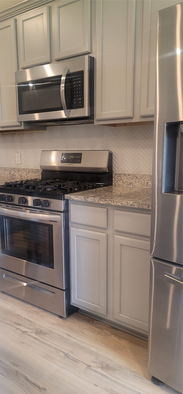 kitchen featuring light hardwood / wood-style floors, appliances with stainless steel finishes, decorative backsplash, and light stone counters