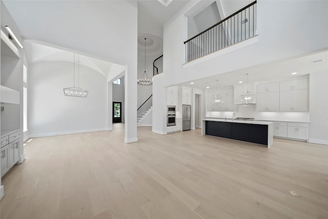 unfurnished living room with a healthy amount of sunlight, a towering ceiling, and light hardwood / wood-style flooring