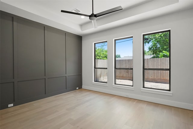 unfurnished room with ceiling fan, a wealth of natural light, a tray ceiling, and light hardwood / wood-style floors