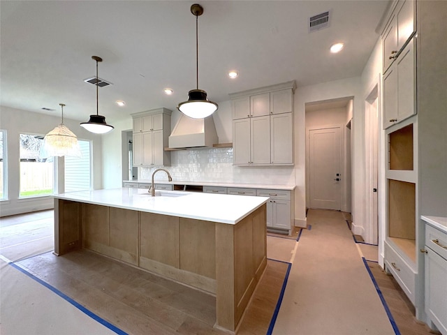 kitchen featuring hanging light fixtures, decorative backsplash, a large island with sink, and premium range hood