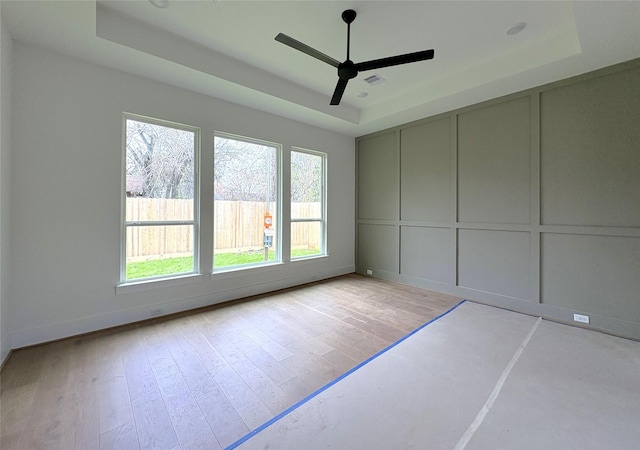 unfurnished room with ceiling fan, light hardwood / wood-style floors, and a tray ceiling