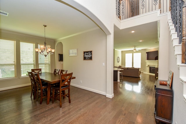 dining area featuring ornamental molding, ceiling fan with notable chandelier, and dark wood-type flooring