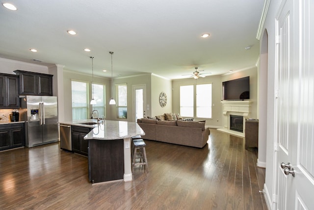 kitchen with a kitchen breakfast bar, stainless steel appliances, dark hardwood / wood-style floors, hanging light fixtures, and an island with sink