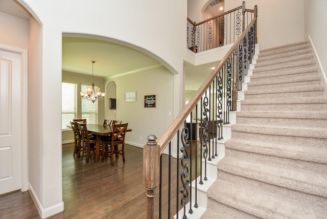 staircase featuring ornamental molding, wood-type flooring, and an inviting chandelier