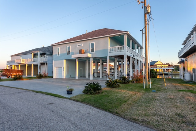 back house at dusk with a garage, a balcony, and a lawn