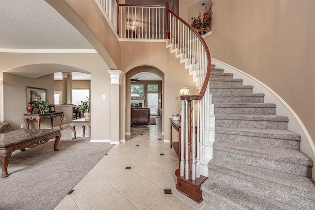 carpeted entrance foyer featuring ornate columns, ornamental molding, and a towering ceiling