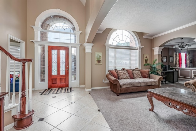 tiled foyer featuring a notable chandelier, crown molding, ornate columns, and a textured ceiling