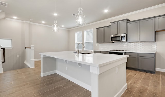 kitchen with gray cabinetry, a kitchen island with sink, sink, light hardwood / wood-style flooring, and stainless steel appliances