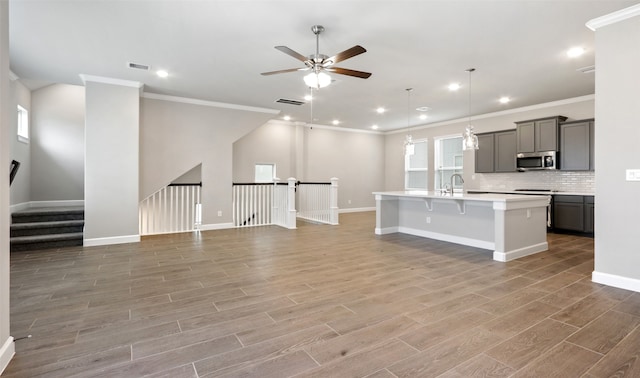 kitchen featuring gray cabinetry, ceiling fan, a breakfast bar, hardwood / wood-style floors, and a center island with sink