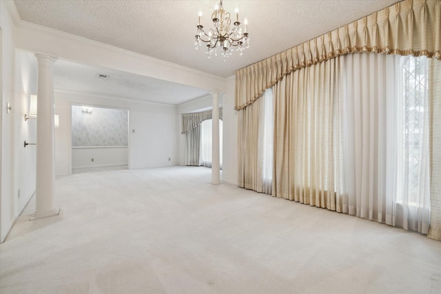 carpeted empty room featuring a textured ceiling, a notable chandelier, ornamental molding, and decorative columns