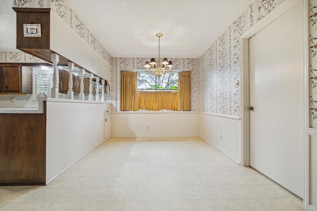 unfurnished dining area featuring a textured ceiling and an inviting chandelier