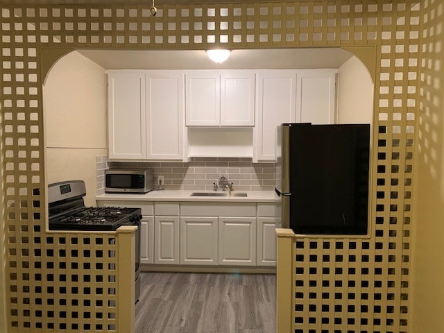 kitchen with appliances with stainless steel finishes, white cabinets, backsplash, light hardwood / wood-style flooring, and sink