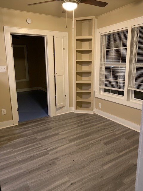 unfurnished room with built in shelves, ceiling fan, and dark hardwood / wood-style flooring