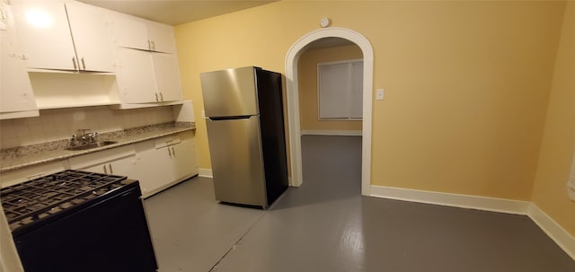3205 Illinois St, Baytown, TX 77520 - kitchen with freestanding refrigerator, black gas range, white cabinetry, decorative backsplash, and arched walkways
