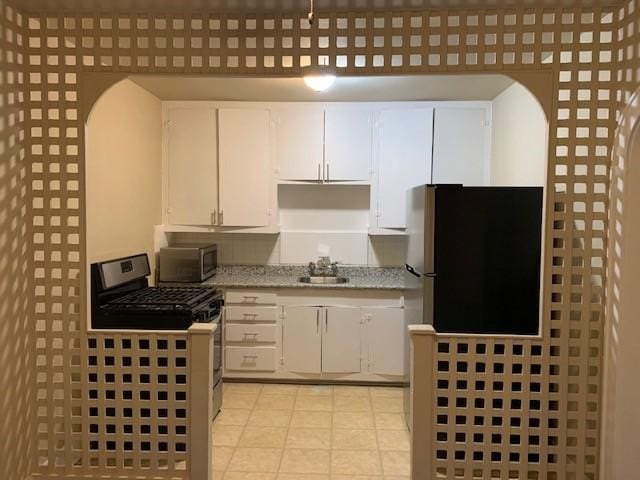 3205 Illinois St, Baytown, TX 77520 - kitchen with stainless steel appliances, white cabinets, light tile patterned floors, light stone counters, and arched walkways