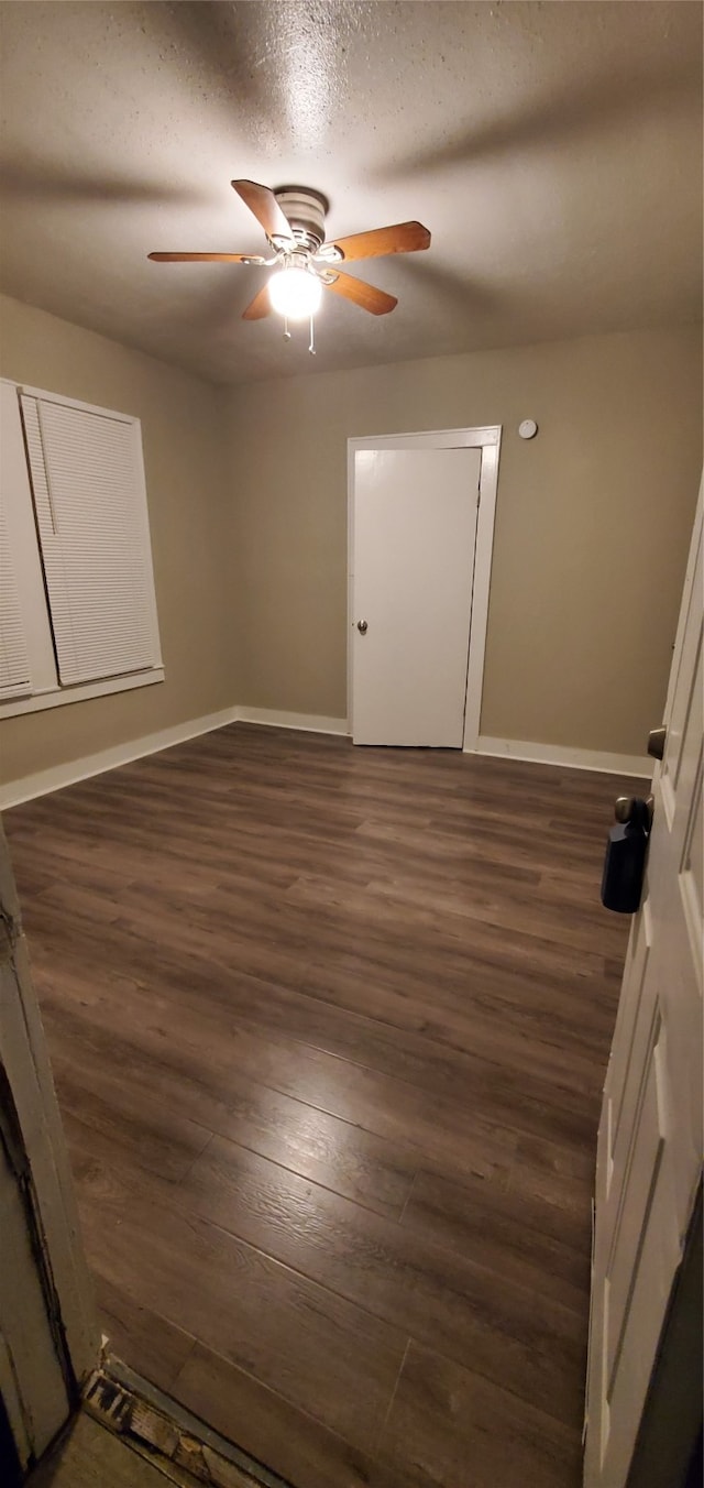 empty room with ceiling fan, dark wood-type flooring, and a textured ceiling