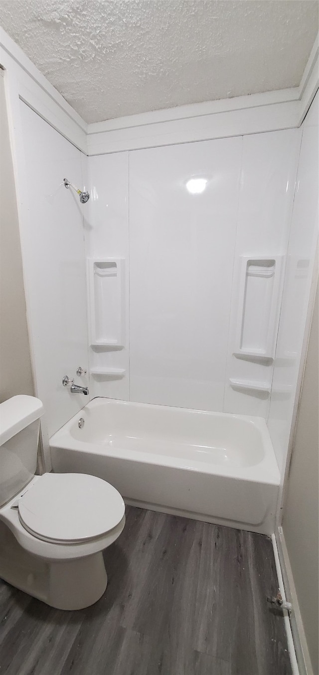 bathroom with a textured ceiling, bathing tub / shower combination, hardwood / wood-style floors, and toilet