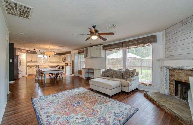 living room with dark hardwood / wood-style flooring, ceiling fan, a stone fireplace, and a textured ceiling