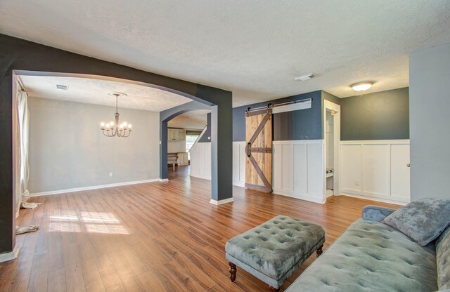 living room with a barn door, wood-type flooring, a textured ceiling, and a notable chandelier